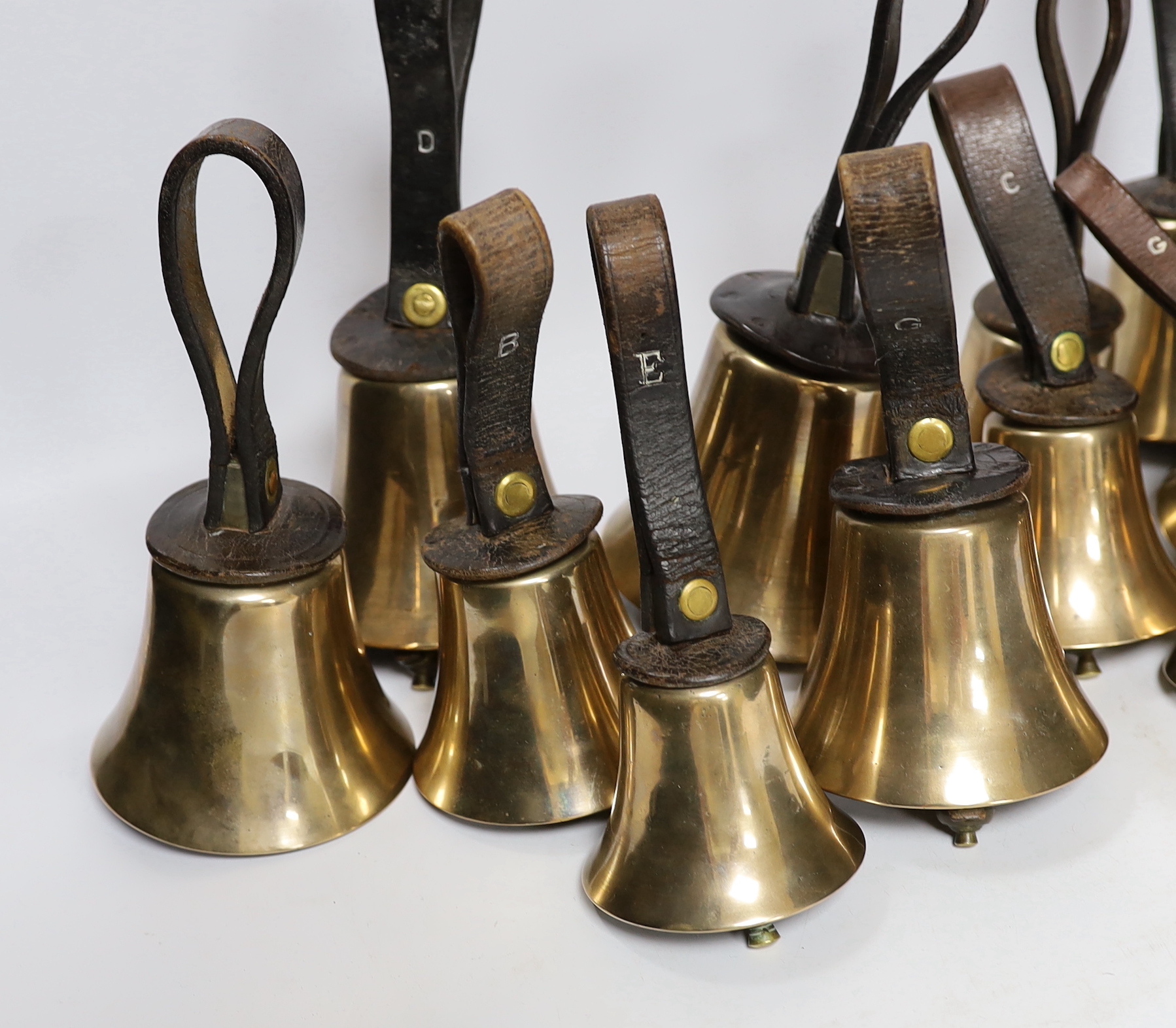 A set of thirty two musical handbells, full chromatic scale, circa 1900, largest 23cm, including leather strap